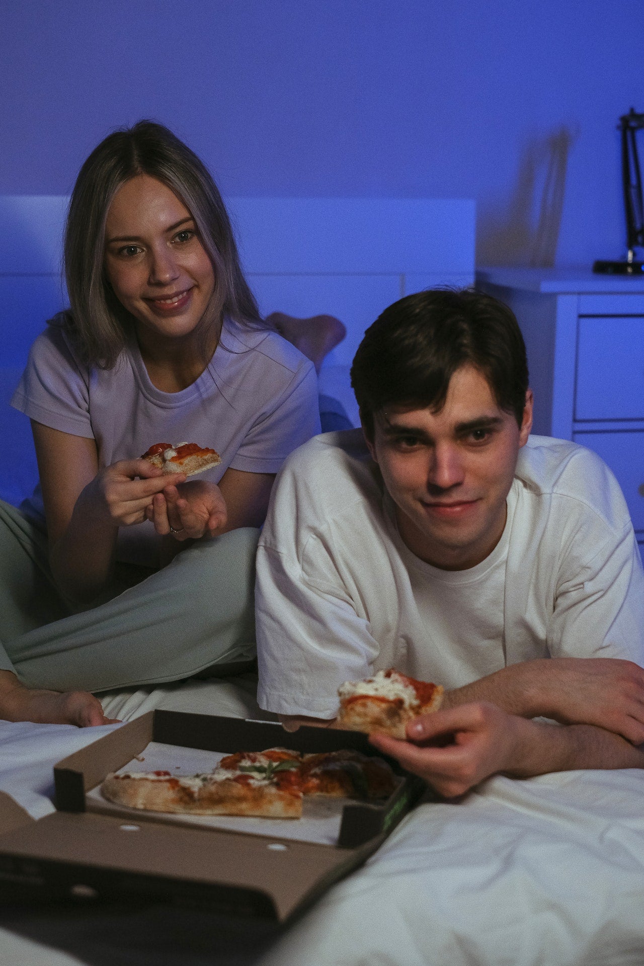 A Couple Eating Pizza while on the Bed