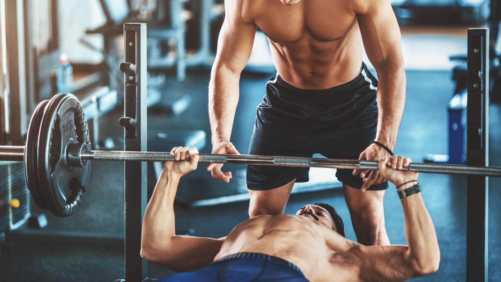 Closeup of mid 20's shirtless man doing bench press exercise in a gym