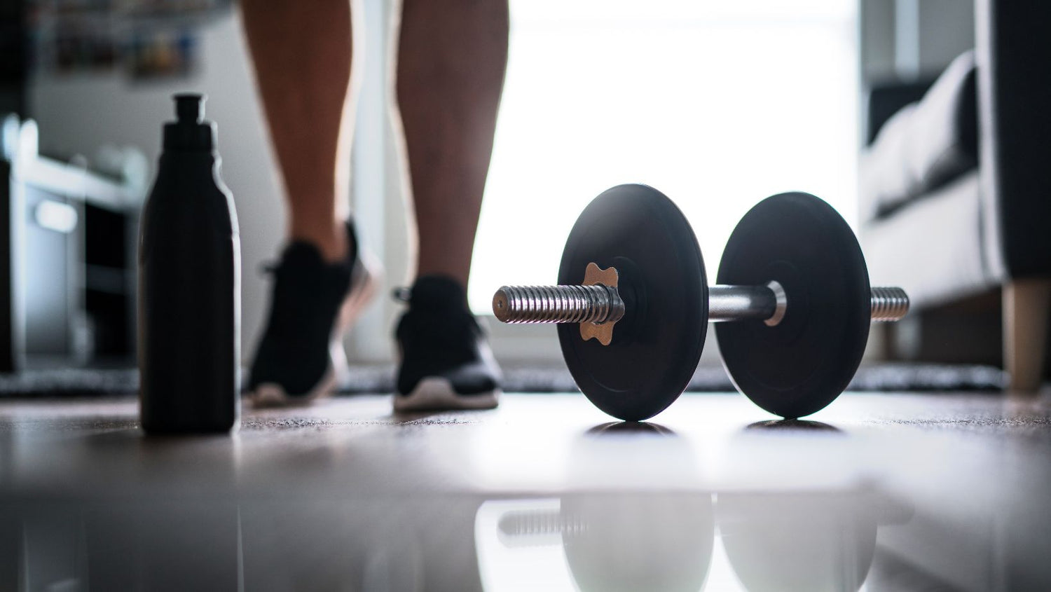 Fitness, home workout and weight training concept. Man starting to exercise with dumbbell. Water or protein shake bottle.