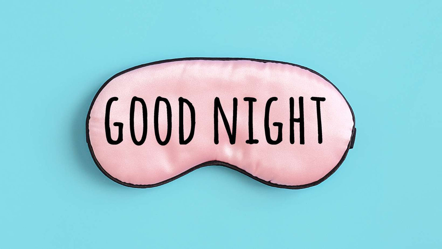 Good night text on pink silk sleep mask for eyes on blue background. Top view Flat lay. Concept eye protection from light for good sleep and melatonin production