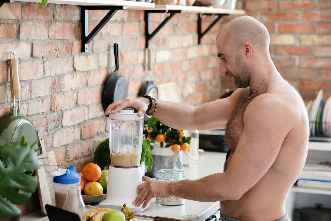 Handsome, shirtless man at kitchen mixing supplements for bulking