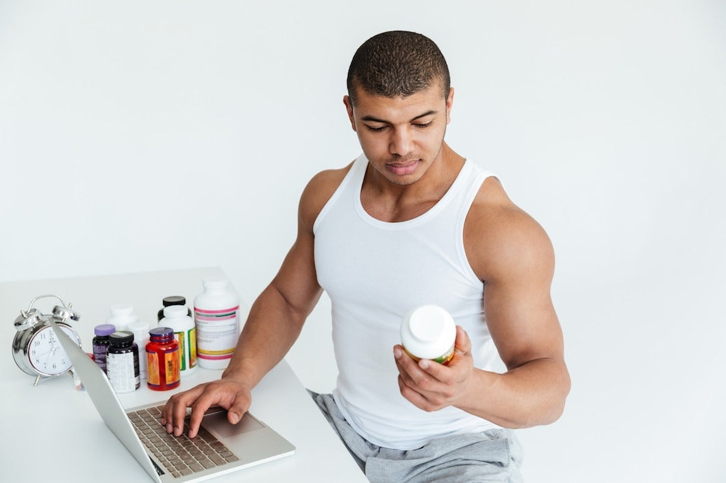 Handsome young sportsman holding sport nutrition and using laptop computer