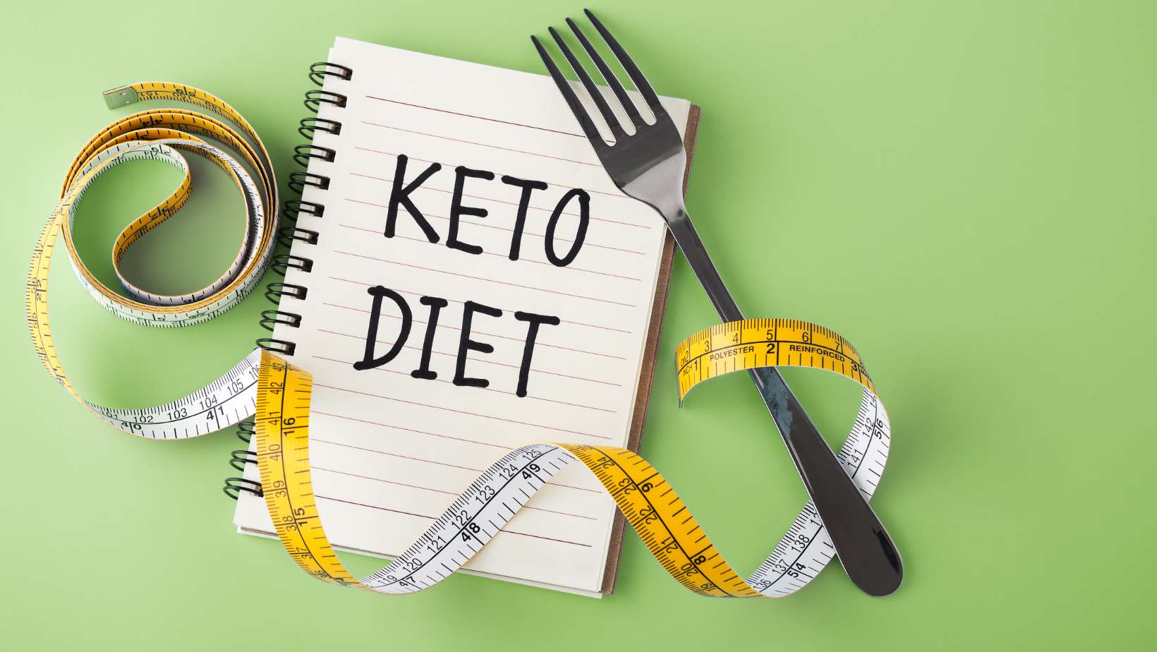 Keto diet word on notebook with measuring tape and fork on green background, top view