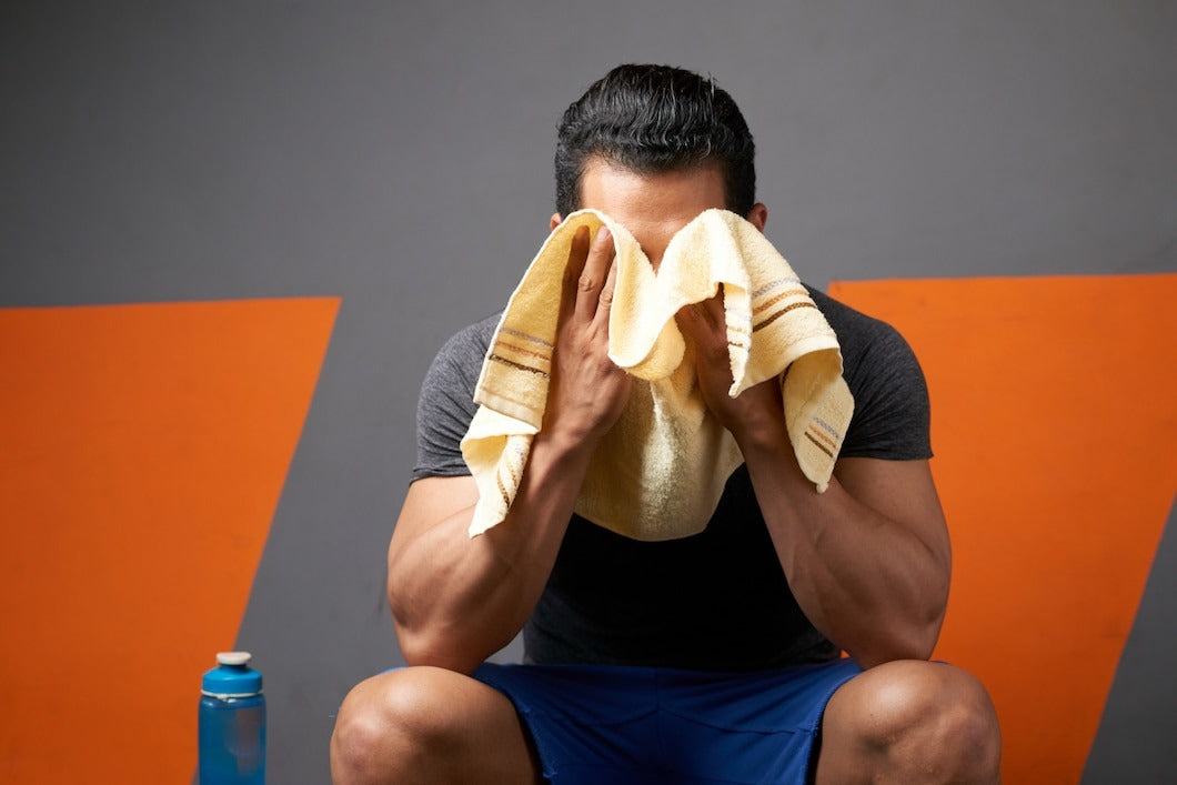 Medium shot of unrecognizable male athlete wiping sweat with a towel seated in gym changing room