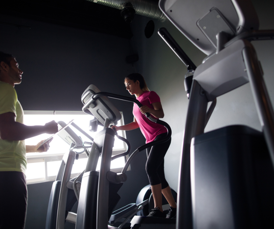 Professional fitness trainer monitoring exercise on elliptical machine