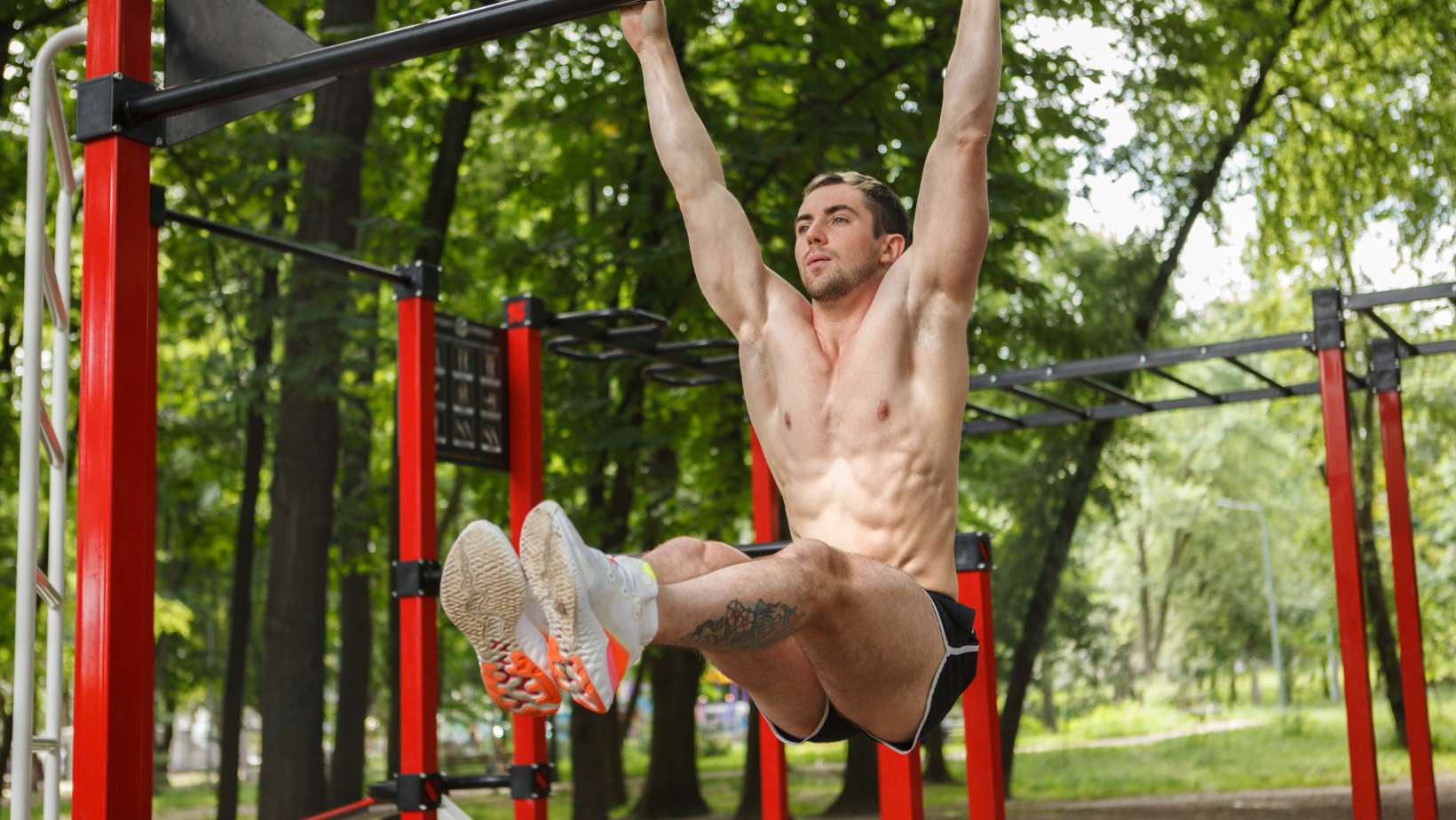 Ripped handsome sportsman exercising outdoors, doing toes to bar abs workout