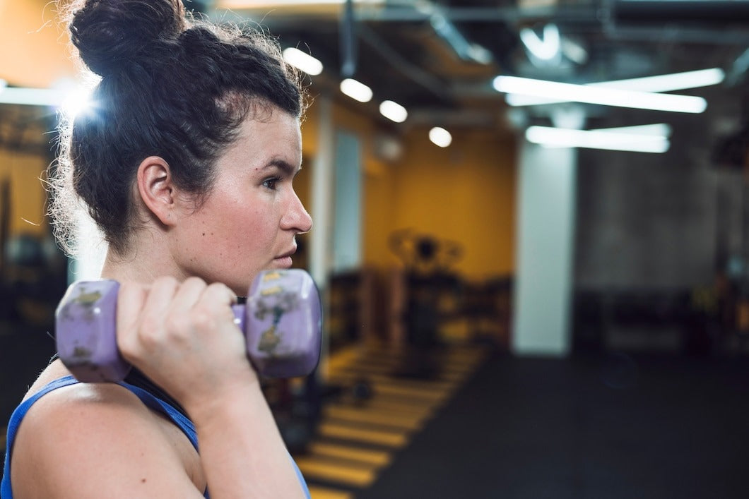 Side view of a young woman doing exercise with dumbbells