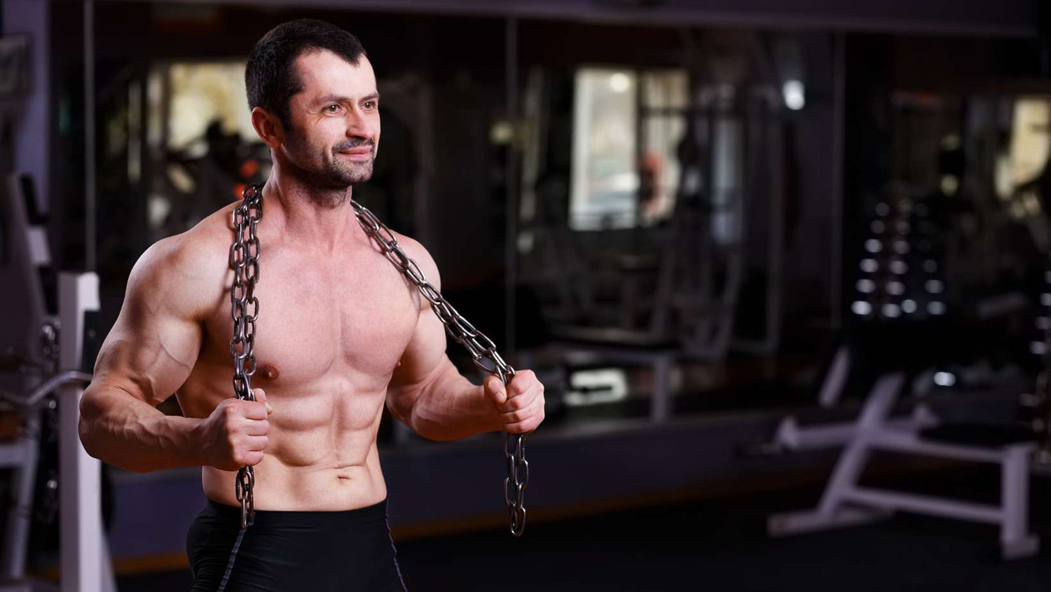 muscular man shirtless holding heavy chain in gym