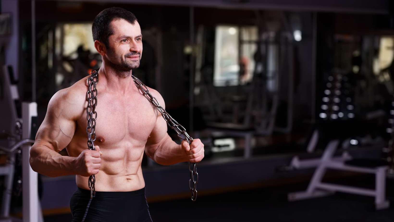 muscular man shirtless holding heavy chain in gym