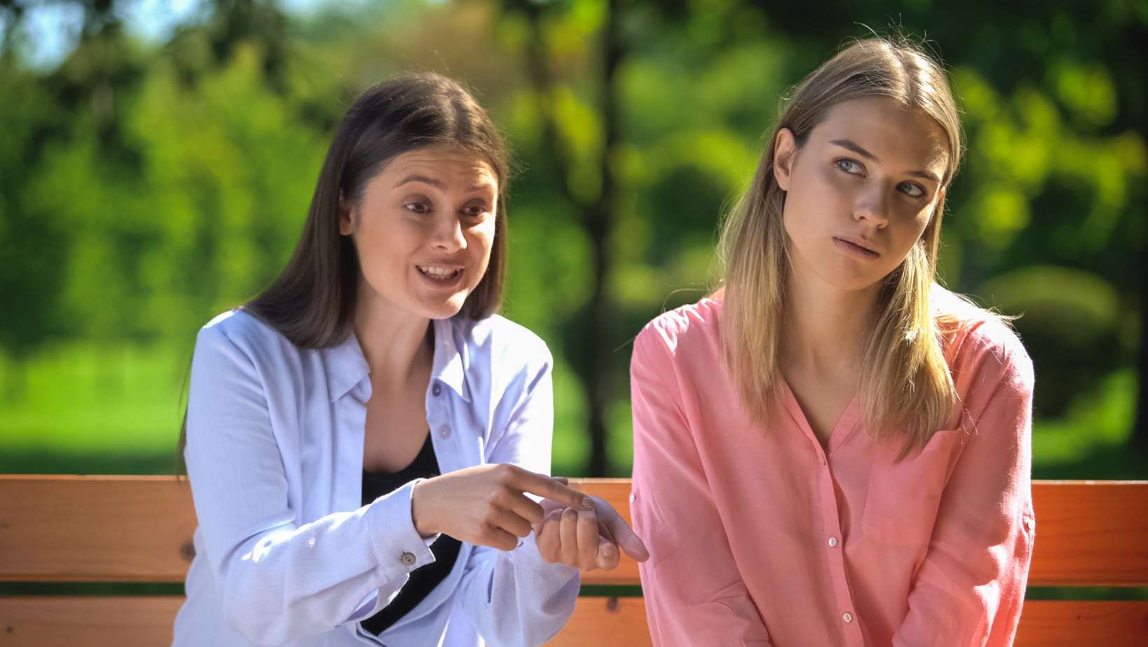 Tired female listening to annoying friend sitting outdoors, envy, selfishness