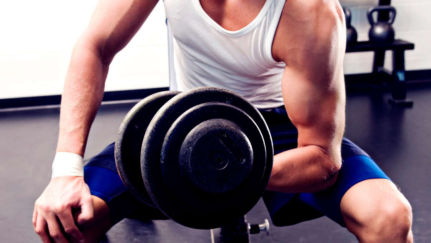 man performing a bicep curl with a dumbbell in a gym. Kettle bells in the background