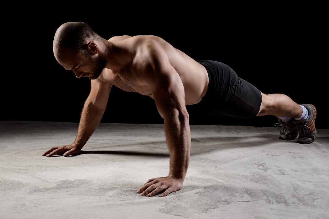 young powerful sportsman planking over dark wall.